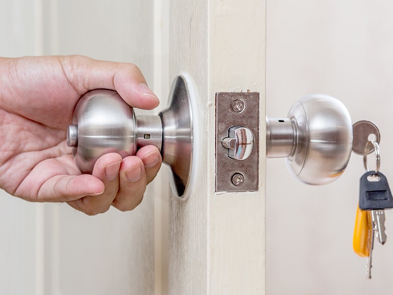 Fotografía de una puerta con una mano en un lado del pomo y unas llaves metidas en el otro lado del pomo.